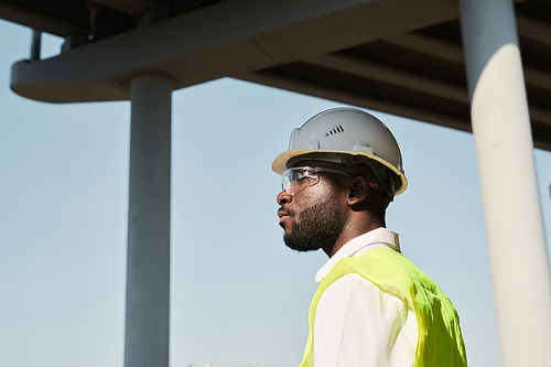 Professional engineer in hardhat in workwear standing at construction site