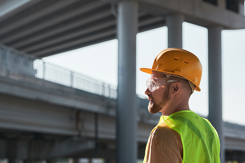 Backlit side view portrait of male construction worker wearing hardhat while standing against sky in background, copy space