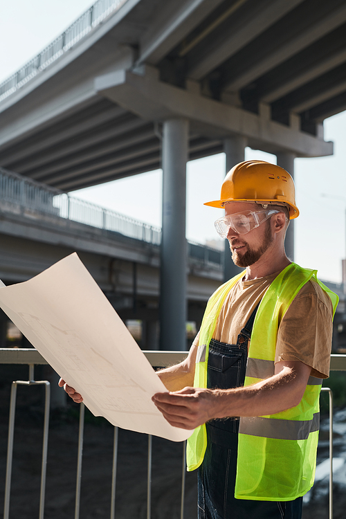 Building worker analyzing project plan and standing on construction site without walls