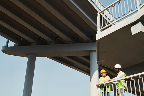 Professional engineers in workwear standing at construction site and discussing building process