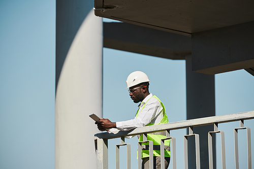 Side view portrait of young black engineer wearing hardhat on construction site against sky, copy space