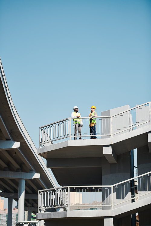 Large construction project in city: busy engineers working with blueprint and standing on construction site of skyscraper without walls