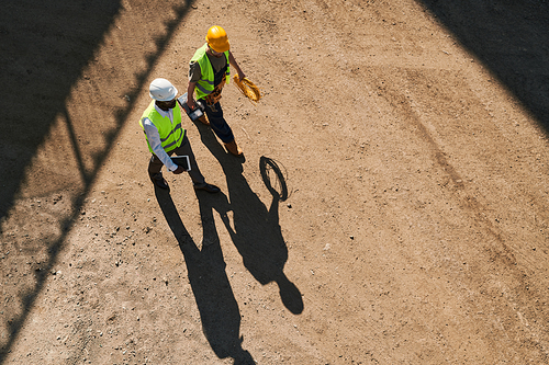 Contemplative modern constructors in safety vests and hardhats working on new house and discussing building process