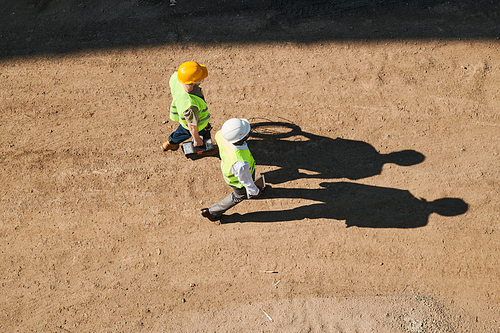 Construction workers examining blueprint and standing on building site of apartment house, large block of flats under construction