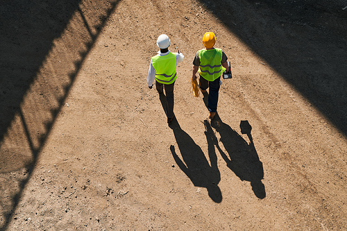 Directly above view of professional engineers in workwear standing at construction site and discussing building process