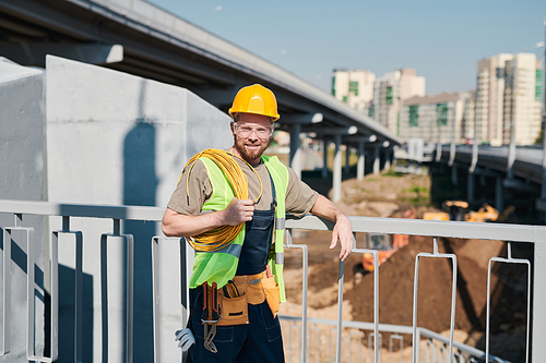 Male construction engineer in white hardhat and green vest contemplating forests and cityscape while choosing place for new building