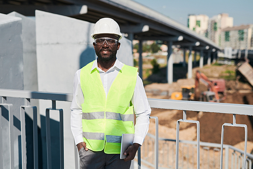 Male construction engineer in white hardhat and green vest choosing place for new building