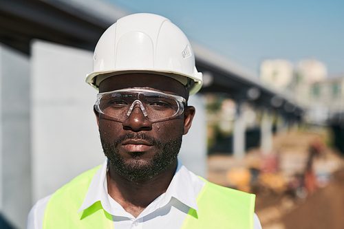 Serious handsome mixed race construction foreman in glasses standing at construction site