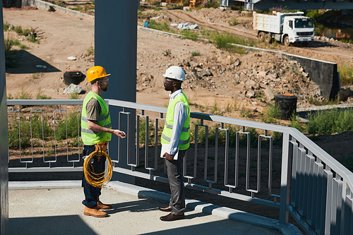 Two construction workers wearing hardhats and chatting while standing against sky in background, copy space