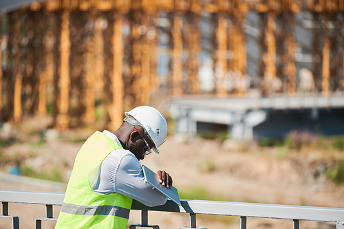 Head and shoulders portrait of bearded construction foreman speaking by walkie-talkie giving instructions to workers on site