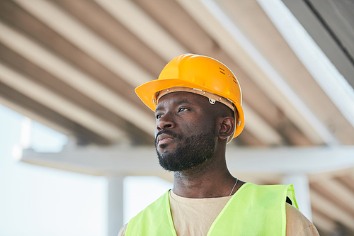 Dramatic portrait of modern construction worker looking away while standing against concrete wall, copy space