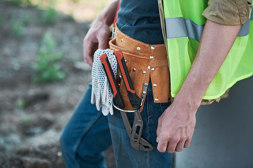 Unrecognizable workman wearing green vest and holding toolbox on construction site