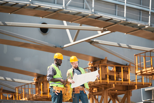 Two construction workers wearing hardhats while chatting at construction site, copy space