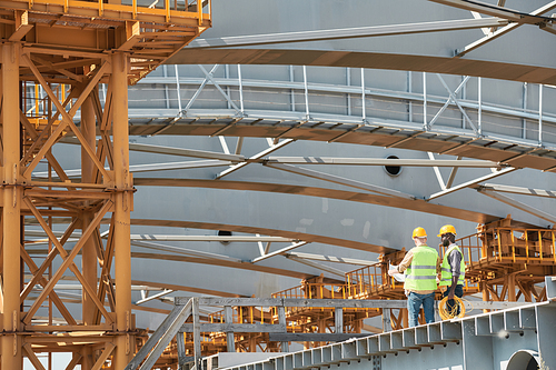 Wide angle view at two workers discussing engineering at costruction site, copy space