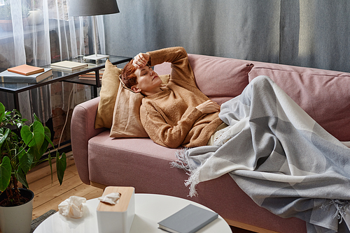 Horizontal high angle view shot of woman lying with eyes closed on sofa at home having fever and headache