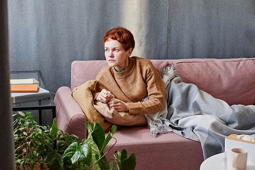 Horizontal shot of mature Caucasian woman with short hair feeling sick holding paper napkin relaxing on sofa at home looking away