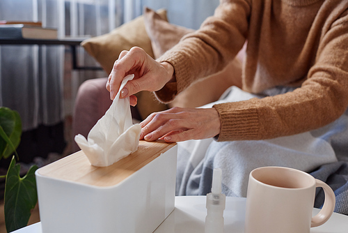 Horizontal close-up shot of unrecognizable woman having cold wearing warm clothes taking fresh paper napkin to blow nose