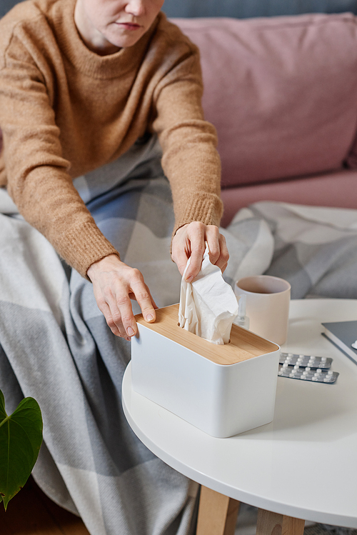 Vertical high angle shot of woman having cold wearing warm outfit staying at home taking fresh paper napkin to blow nose