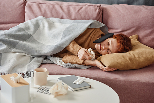 Horizontal medium shot of mature Caucasian woman having influenza lying on sofa having phone call