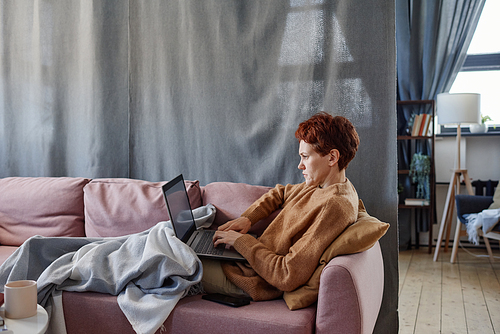 Horizontal side view shot of mature Caucasian woman having influenza staying at home working on laptop