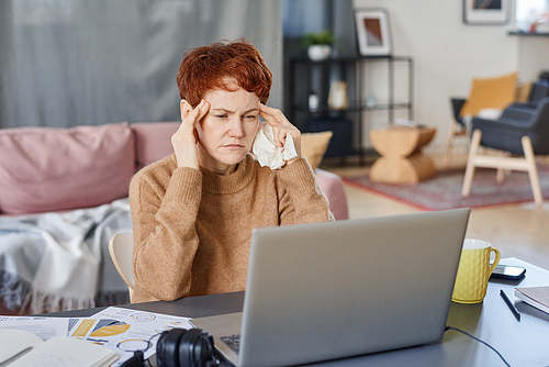 Horizontal shot of mature Caucasian manager suffering fever with headache staying at home sitting at desk working on laptop