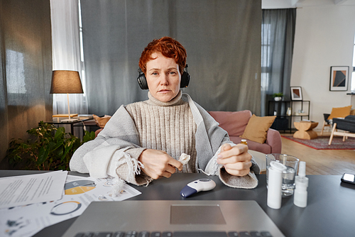 Horizontal shot mature woman sitting at desk in living room at home telling physician about symptoms during online appointment