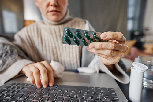 Horizontal shot of mature Caucasian patient sitting at desk in front of laptop showing pills to doctor during online consultation