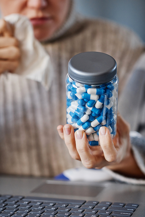 Vertical selective focus close-up shot of mature Caucasian patient sitting at desk in front of laptop showing pills to doctor