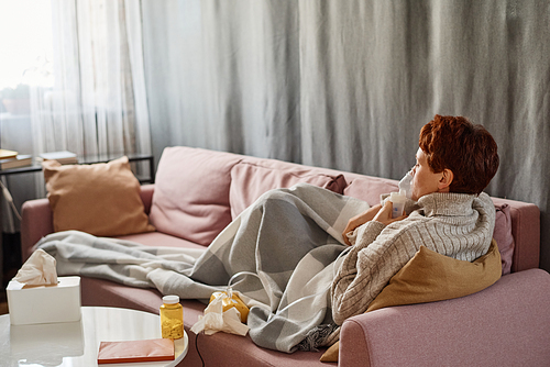 Horizontal shot of modern mature Caucasian woman having influenza staying at home relaxing on sofa using nebulizer