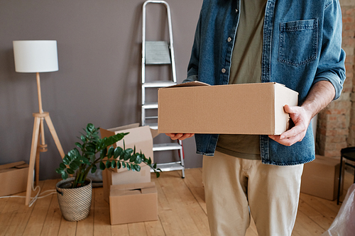 Horizontal shot of unrecognizable young man wearing casual clothes bringing boxes with things to new apartment