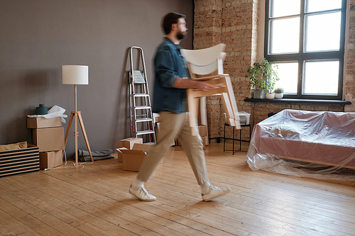 Horizontal side view shot of young Caucasian man moving to new apartment bringing chairs into it