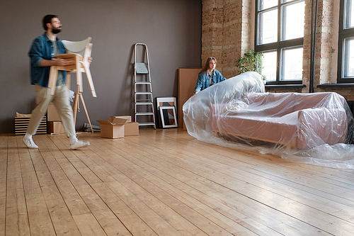 Horizontal long shot of young man and woman getting ready to move to new house packing things and furniture