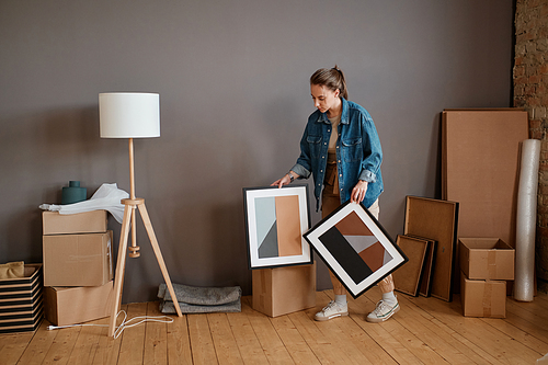 Horizontal shot of young woman moving to new house taking abstract paintings to wrap and pack them