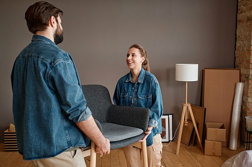 Horizontal shot of modern young man and woman in love moving to new apartment carrying furniture together