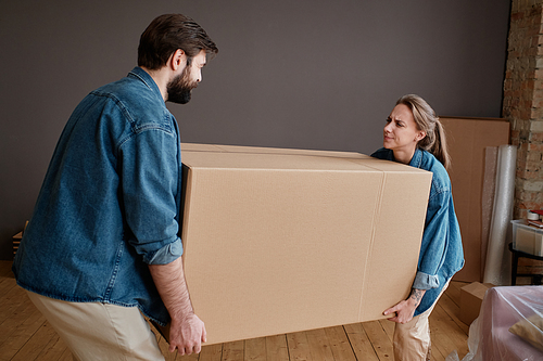 Horizontal shot of young man and woman moving to new apartment carrying big heavy box together