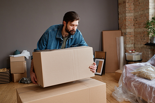 Horizontal shot of young man moving to new apartment bringing and placing boxes with stuff in there