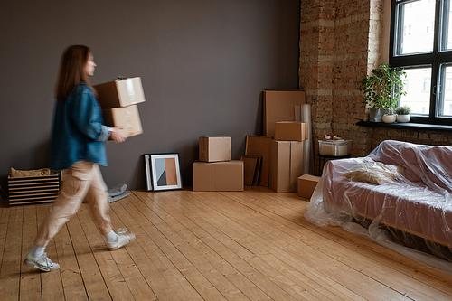 Horizontal long shot of young woman moving to new apartment bringing boxes with stuff