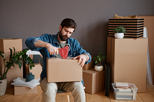 Horizontal shot of young man with beard on face sitting on chair getting ready for moving to new house