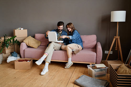 Young man and woman relaxing together on sofa eating pizza in loft living room after moving to new house