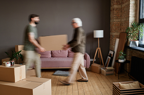 Horizontal long shot of young son helping his senior father with moving to new house carrying boxes full of stuff together