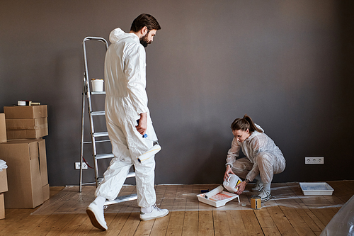 Modern young man and woman wearing protective clothes doing repair work in their apartment going to paint wall