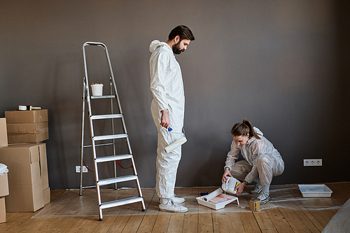 Young couple wearing protective clothes doing repair work in their new apartment getting ready to paint wall