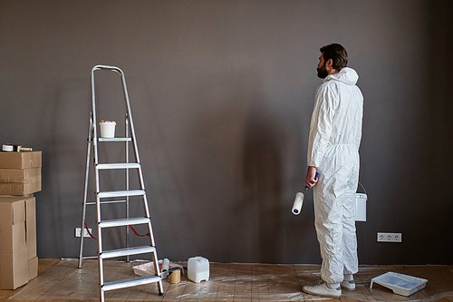 Young Caucasian man wearing protective clothes doing renovating works in new apartment going to paint walls