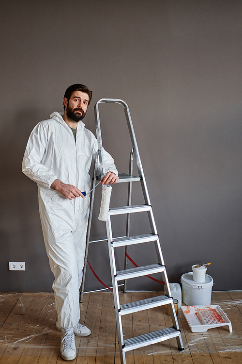 Vertical shot of Caucasian man wearing protective outfit doing renovating works in his apartment looking at camera