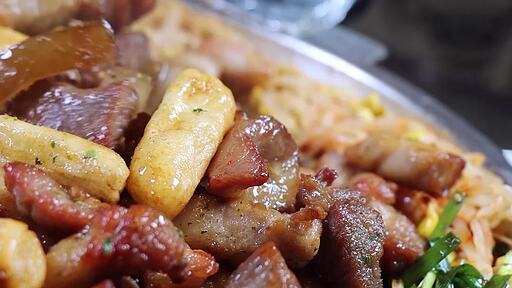 삼겹살 돼지껍질과 떡을 돌판 위에서 지글지글 볶아 미나리와 콩나물을 곁들여 먹는 모습