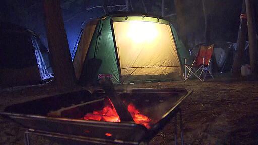 켐핑장에 피워놓은 모닥불 뒤로 보이는 텐트의 불이 꺼지는