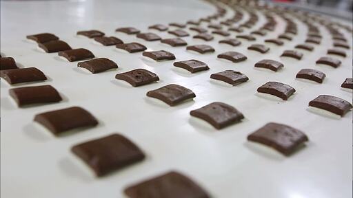 갈색의 초콜릿들이 움직이는 제조 기계에서 대량으로 만들어지고 녹은 초콜릿이 굳은 초콜릿에 뿌려지는