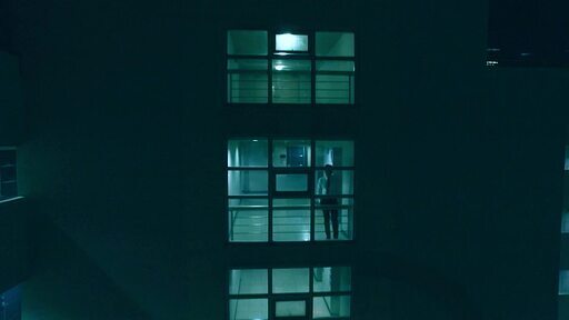 어두운 건물안에 서 있는 넥타이를 맨 남자와 건물 넘어로 보이는 화려한 서울 고층 빌딩이 대비되는
